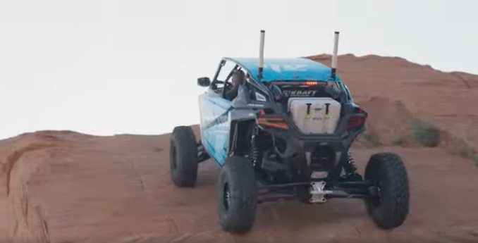 Still from a campaign video of an off-road vehicle climbing red rock with a Lifetime cooler strapped to the rack